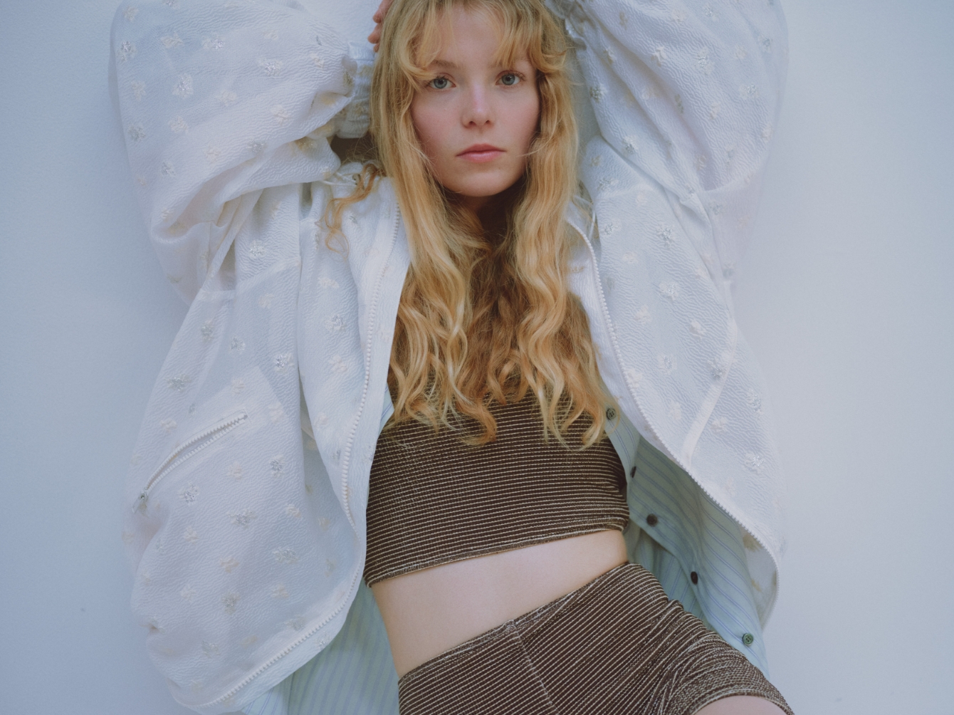 ビッグフォルムフーディーブルゾン、ストライプベーシックシャツ、シュシュ付きバンドゥスイムウェア、シアーハイソックス、メリージェーンスニーカーを着用した女性モデル