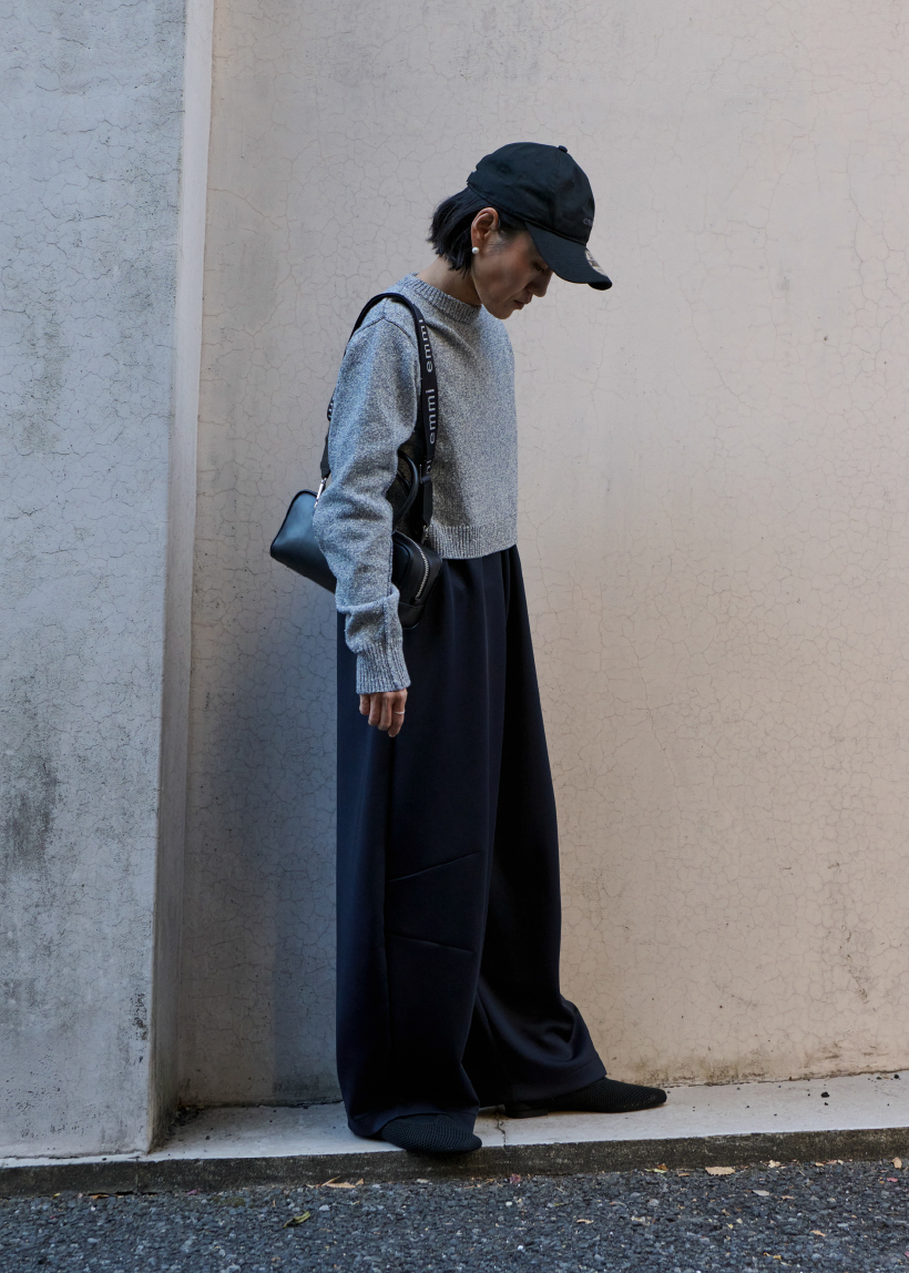 ecoラメニットプルオーバー・ecoダンボールコクーンコンビネゾン・【emmi|NEW ERA®】9TWENTY™emmiロゴキャンバスキャップ・ecoウォッシャブルメッシュニットフラットシューズを着用した女性